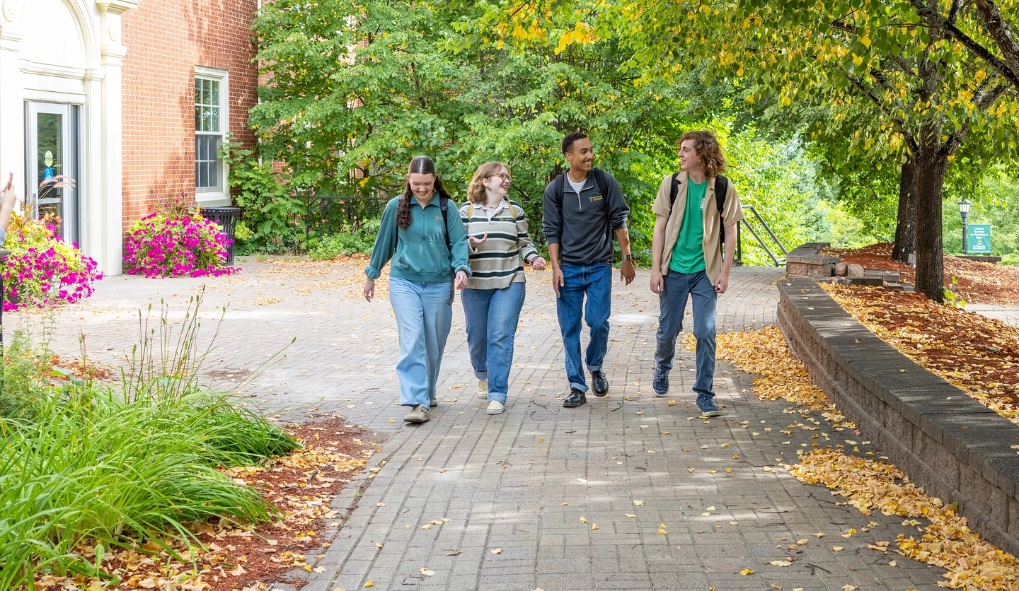 Two female students and two male students walk through lower campus talking to one another