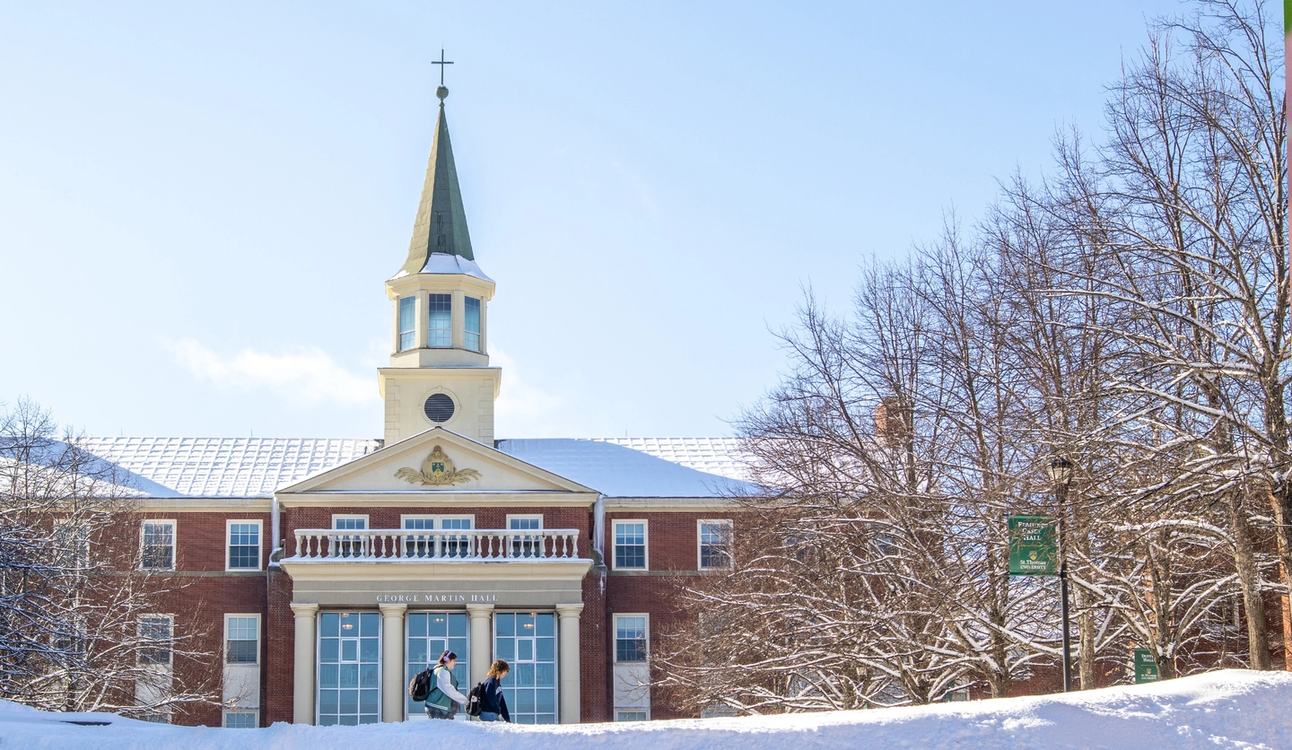 Two students walk in front of George Martin Hall on a snowy winter day