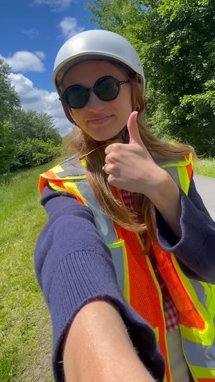 Emily gives a thumbs up while wearing a helmet and orange safety gear before an e-bike site visit.