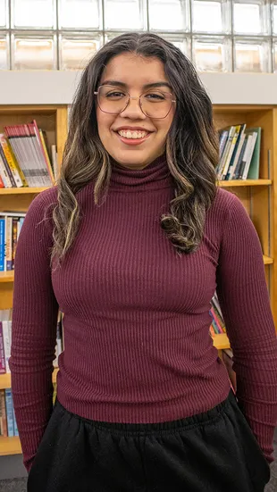 A photo of a female student in front of a bookshelf