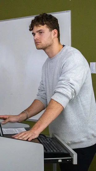A male student stands behind a podium in a classroom