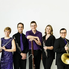 The group Ventus Machina stands holding their instruments in front of a white backdrop