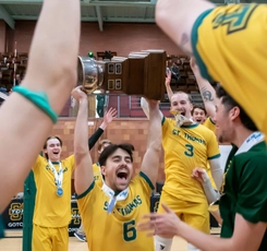 A group of men's volleyball players celebrate while hoisting the championship trophy