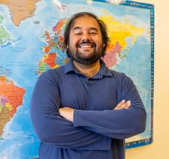 2026 Valedictorian Ameya Charnalia standing in front of global map in classroom