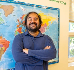 2026 Valedictorian Ameya Charnalia standing in front of global map in classroom