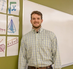 Brent Standing in classroom next to white board math posters