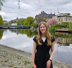 A student on exchange in Sweden stands near a river, surrounded by greenery