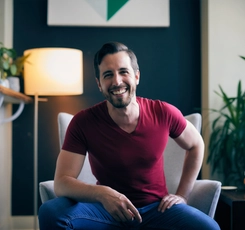 STU alumnus Mark Henick sits in a gray chair in front of a lamp