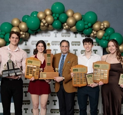 Two male students and two female students stand holding trophies and plaques with university President Dr. Nauman Farooqi