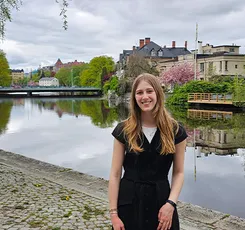 A student on exchange in Sweden stands near a river, surrounded by greenery