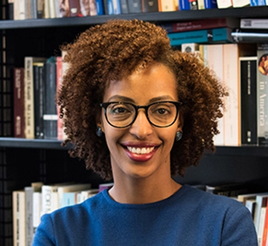 Dr. Adom Getachew standing in front of a bookcase