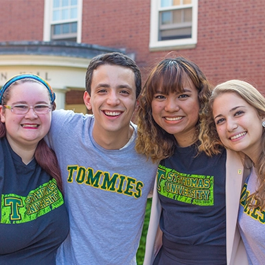 Group of four students huddled together and smiling for the camera