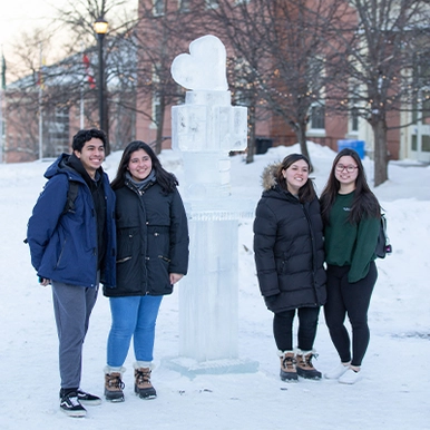 Four students in the winter outside in lower courtyard next to an ice sculpture
