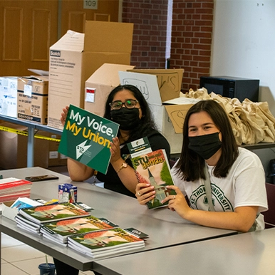 Two students sitting at Welcome booth and waving a STU flyer and STU genda