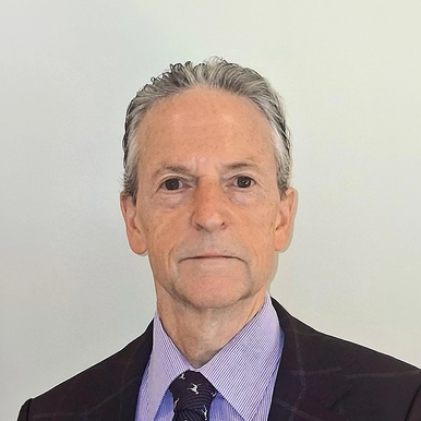 Dr. Rick Myers stands in front of a gray wall wearing a blue suit