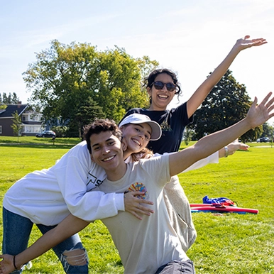 Three students volunteering outdoors, waving and smiling for photo