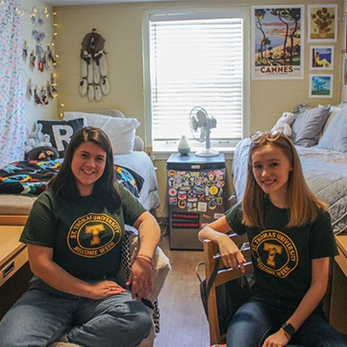 Two students smiling and sitting at their desks in dorm room.