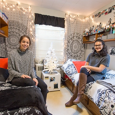 Two students sitting on their dorm beds smiling