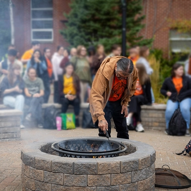 Elder in Residence Ron Tremblay tends to the fire at the Sacred Fire Pit on campus