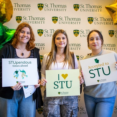 Three female students standing in front of 911������ Banner with accepted to 911������ signs
