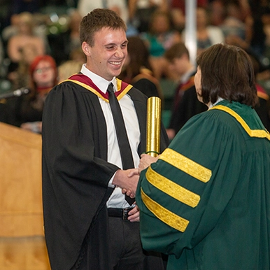 Student shaking hands with STU president and receiving diploma at Convocation ceremony