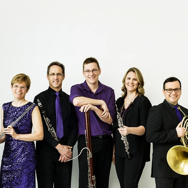The group Ventus Machina stands holding their instruments in front of a white backdrop