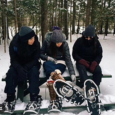 Three students wearing snowshoes sitting in the forest.