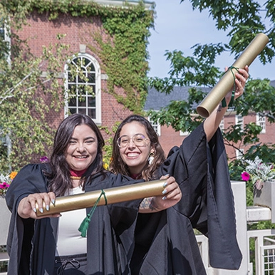 To graduates wearing their robes hold up their diploma tubes