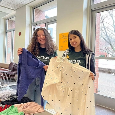 Two STUdents stand holding up shirts from a previous sustainability swap