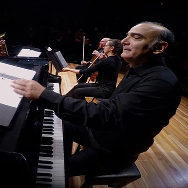 Fine Arts professor Martin Kutnowski sits at a piano on a stage with members of the Saint John String Quartet in the background. Screenshot from documentary trailer from Silver Wave Film Festival.