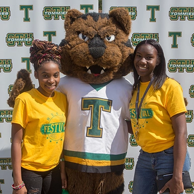 Two students standing next to the STU mascot