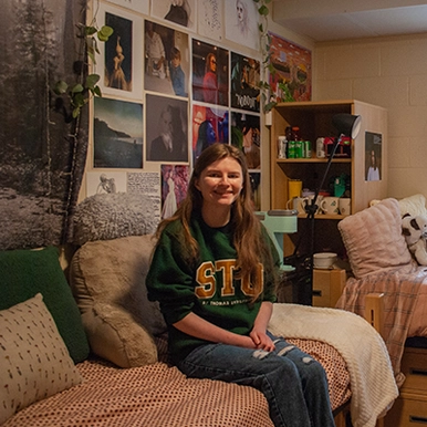 Student sitting on bed in dorm room