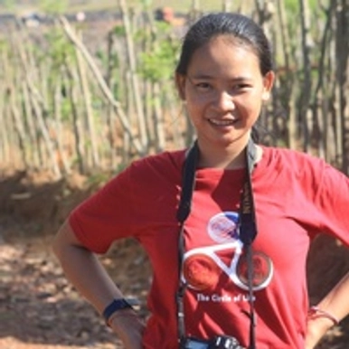 A woman wearing a red t-shirt standing in front of a field