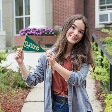 A smiling student holding a STU pennant