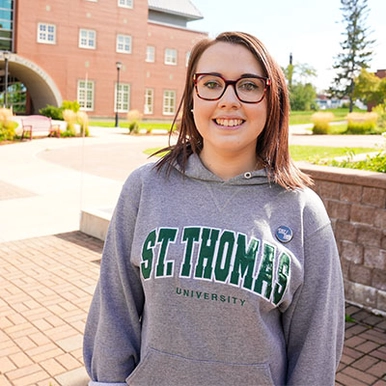 A student wearing a STU hoodie standing in courtyard