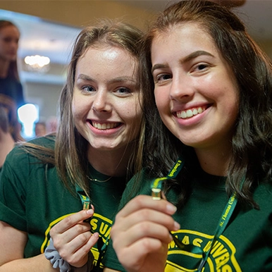 Two students in green shirts holding up their T pins