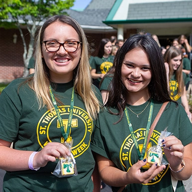 Two students stand next to each other wearing STU shirts and holding up their T-Pins