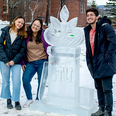 A photo of three students around an ice sculpture on campus