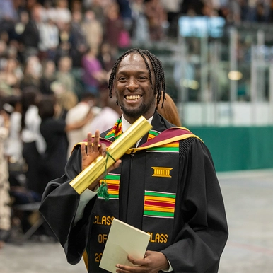 A male graduate smiles and waves at the camera
