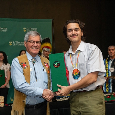 The Hon. Graydon Nicholas, presents a graduating student with an eagle feather that's encased in a green embroidered folder.