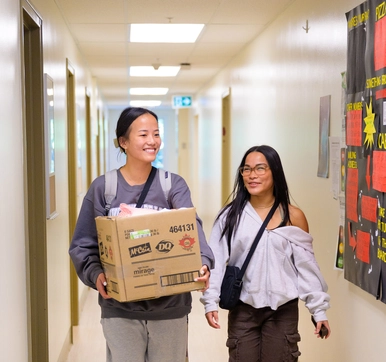 A female student walks down the hall holding a cardboard box alongside her mom, who is smiling at her.