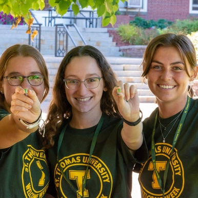 Three students at welcome week holding up T pins