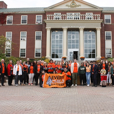 Students wearing orange with an Every Child Matters sign in front og George Martin Hall