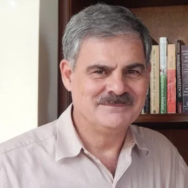 Headshot of Dr. Juan Alberto Fuentes Knight next to a bookshelf