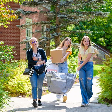 Three women moving boxes into residence