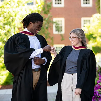 Two students in graduation gowns fist bumping