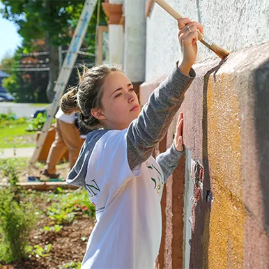 Student painting wall outside for STU Cares day