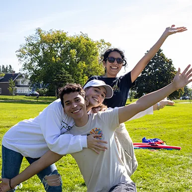 Three students volunteering outdoors, waving and smiling for photo