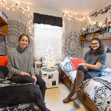 Two students sitting on their dorm beds smiling