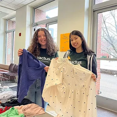 Two STUdents stand holding up shirts from a previous sustainability swap